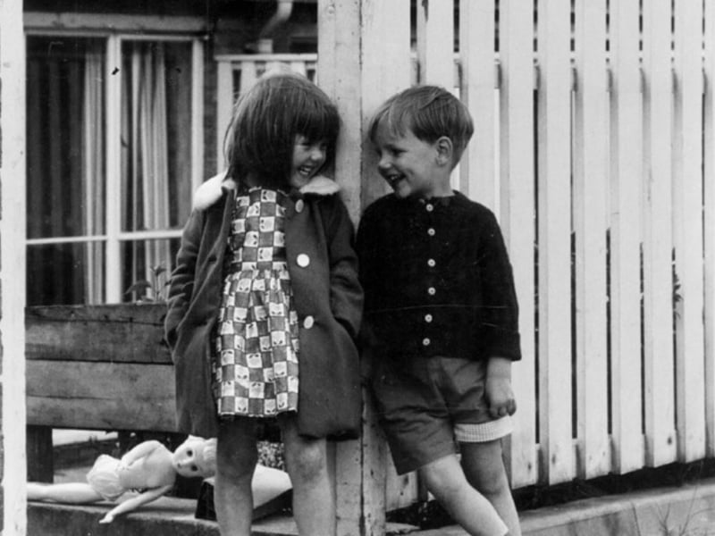 Two children laughing together outside a house, believed to be on Raeburn Road, Herdings, Sheffield, during the 1960s