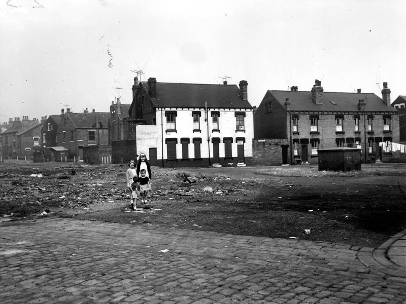 Vicar Street, Leeds, viewed across a section of waste ground towards Selborne Place. Four children of varying ages stand in the centre of the photo, taken in September 1964. The terraces seen on the far left are Berwick Place and Berwick Terrace, and the white building behind the children is number 16 Selborne Place, the Progressive Christian Spritual Church. On the right is a yard and numbers 10 to 14 Selborne Place. These houses were soon to be demolished and families relocated under a Leeds City Council slum clearance