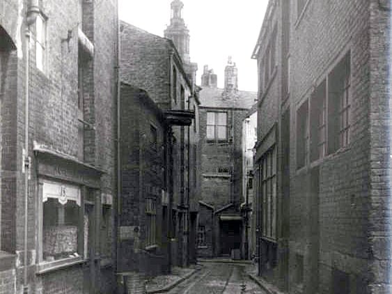 Anchor Court was located off the west side of the Market Place. This view looks east towards the Market Place with the tower of the Sessions House on the skyline.
The premises of J. Sharples and Company, upholsterers, on left. All these properties were swept away in 1962 to make way for St. George's Shopping Centre.