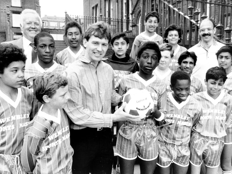 England and Manchester United captain Bryan Robson at Harehills Middle School, Leeds, in May 1987. He presented the school football team with a complete strip donated by Wembley Sportsmaster Ltd, and a soccer ball which he is seen handing to team captain Donovan Daniel.