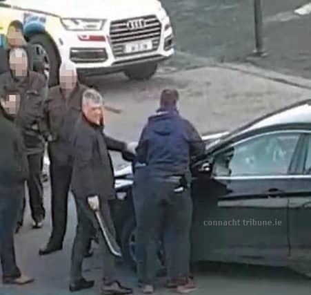 An armed plainclothes detective hold a machete with a two-foot blade, while another detains a man at the funeral.