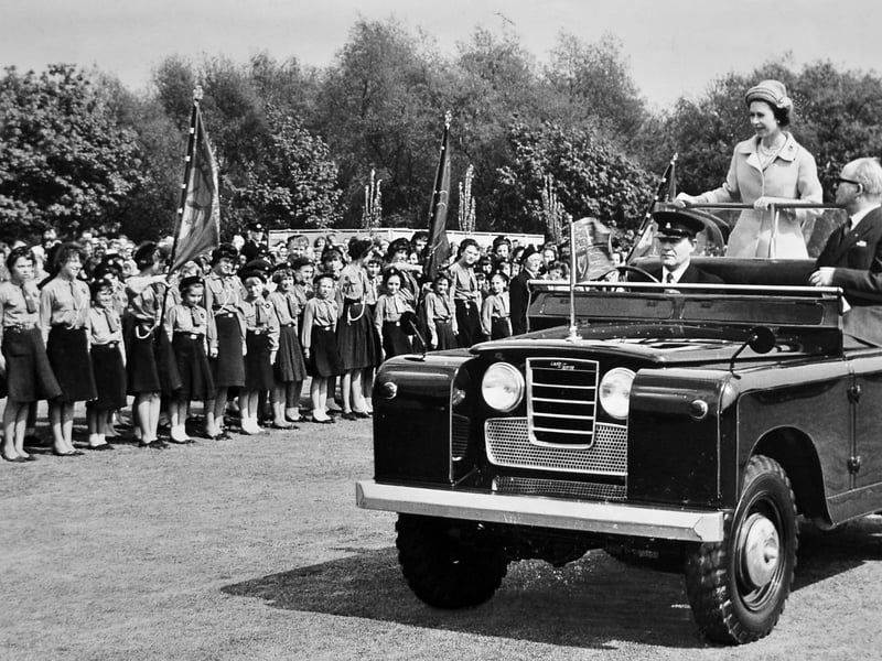 Queen Elizabeth II stands in an open-top Land Rover as it moves slowly past cheering crowds at Walsall Arboretum on May 24, 1962. Around 5,000 members of local youth organisations, including Scouts, Guides, and youth groups lined up with banners to greet the Monarch during her royal visit to the Black Country. The joyous event brought thousands of families and young people together in the park, creating an unforgettable moment in Walsall's civic history. Were you among the 5,000 young people at the Arboretum or do you remember watching the Queen's visit to Walsall in 1962?