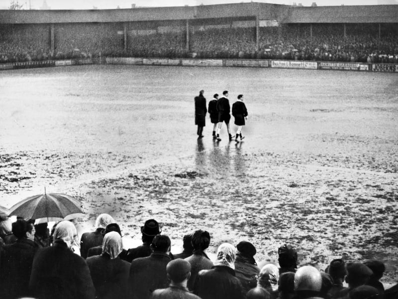 Referee Gordon Roper and his linesmen wade across a completely submerged pitch at Fellows Park in May 1963. This striking photo reveals the aftermath of a sudden half-time deluge that brought an abrupt end to the Walsall versus Charlton Athletic fixture. Devoted Saddlers supporters huddled under umbrellas and rain bonnets on the terraces as official pitch inspections confirmed what everyone already knew—the turf had turned into a proper swimming pool. Were you standing on the terraces at Fellows Park when this torrential downpour washed out the match?
