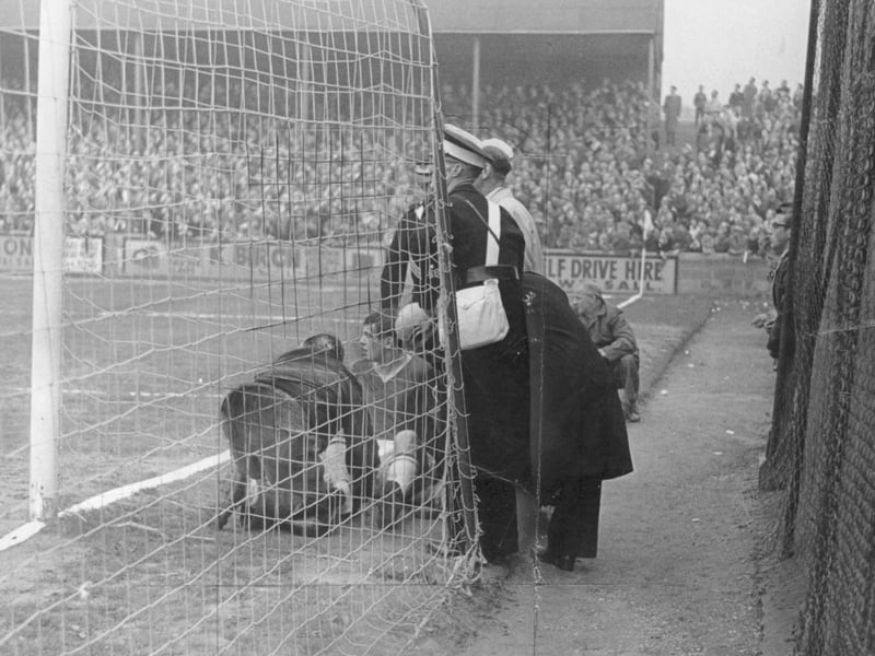 St John Ambulance attendants and a trainer rush to assist an injured player seated behind the goal netting during a match at Walsall FC's former home, Fellows Park. Packed terraces look on in suspense as first aid is administered right on the touchline, framed by classic advertising hoardings promoting local Walsall businesses like Self Drive Hire. Action-packed moments like this captured the raw, intimate atmosphere of lower-league football, where supporters stood just yards away from the pitch and touchline medical care was far more straightforward than today. Does this scene bring back memories of cheer and tension on the terraces at Fellows Park?