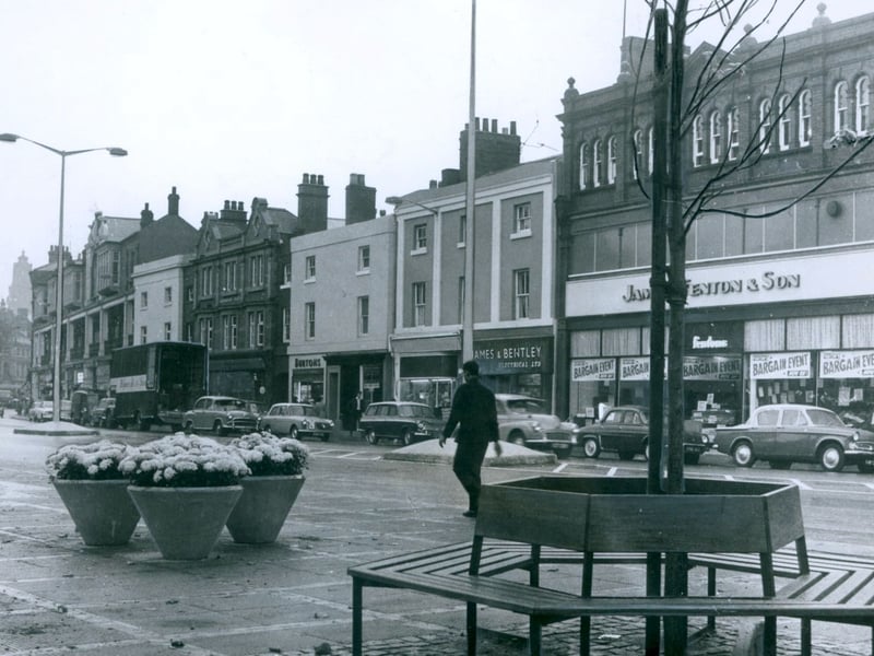 Fresh flower tubs, new street lighting, and a circular wooden bench take centre stage along Bradford Street in Walsall during September 1963. The smartened-up thoroughfare is pictured on the very day a major civic facelift scheme was officially launched to brighten up the town centre. Showcasing bustling storefronts like James & Bentley Electrical Ltd alongside classic saloons parked along the kerb, the photograph captures a proud moment of urban renewal for local shoppers and traders. Do you remember browsing the shops along Bradford Street after the new street furniture was installed?