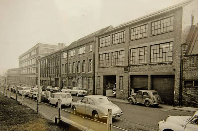 Classic 1960s saloons line the kerb outside the bustling Yale Lockworks on Wood Street, Willenhall, in this 1962 industrial snapshot. Long celebrated as the lockmaking capital of the country, Willenhall was home to the world famous Yale brand, which operated massive manufacturing premises in the heart of the town. The photograph shows open loading bays, brick factory facades, and workers' cars parked along the street during the height of the region's manufacturing boom. Did you or anyone in your family work at the Yale Lockworks on Wood Street back in the 1960s?