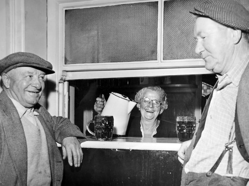 Framed by flat caps and dimpled glass mugs, a cheerful landlady pours a drink through a traditional pub serving hatch in Shrewsbury, likely captured between the late 1950s and early 1960s. Though the exact location and the identity of the locals remain unknown, the lively atmosphere perfectly preserves the simple pleasure of an after-work pint and a friendly bit of banter in a classic Shropshire local. Do you recognise this cosy serving hatch, or do you remember frequented pubs around Shrewsbury from this era?