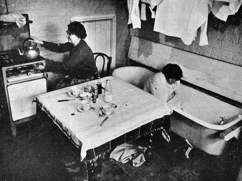 Mrs May Groucott is pictured putting the kettle on in the tiny kitchen of her council house in Regent Street, Wellington, on February 26, 1965. The room also served as the bathroom, while behind her was the coal cellar. Her neighbour, Mrs Ursula Hickman, demonstrates just how basic bathtime could be, with only a single tap supplying cold water. The photograph offers a striking glimpse of everyday life in Wellington at a time when some families were still living with very basic facilities. Do you remember homes like this in the 1960s? Did you grow up with a coal cellar or remember having a bath from a cold-water tap?