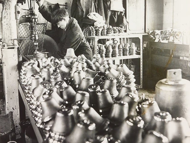 Surrounded by rows of freshly cast handbells, 16-year-old Malcolm Shaw operates a pillar drill at Edwin Preston Ltd on Jenner Street in Wolverhampton on June 24, 1970. Malcolm, who lived nearby at Hazel Grove in Bilston, worked amidst shelves and workbenches stacked high with gleaming metal bells waiting to be drilled, polished, and assembled. The workshop scene offers a wonderful glimpse into the specialised manufacturing trades and youth apprenticeships that flourished across local industrial firms during the 1970s. Do you remember Edwin Preston's foundry or the brass-founding tradition around Wolverhampton and Bilston? Did you or a family member start a apprenticeship at a local workshop right after leaving school in the 1970s?