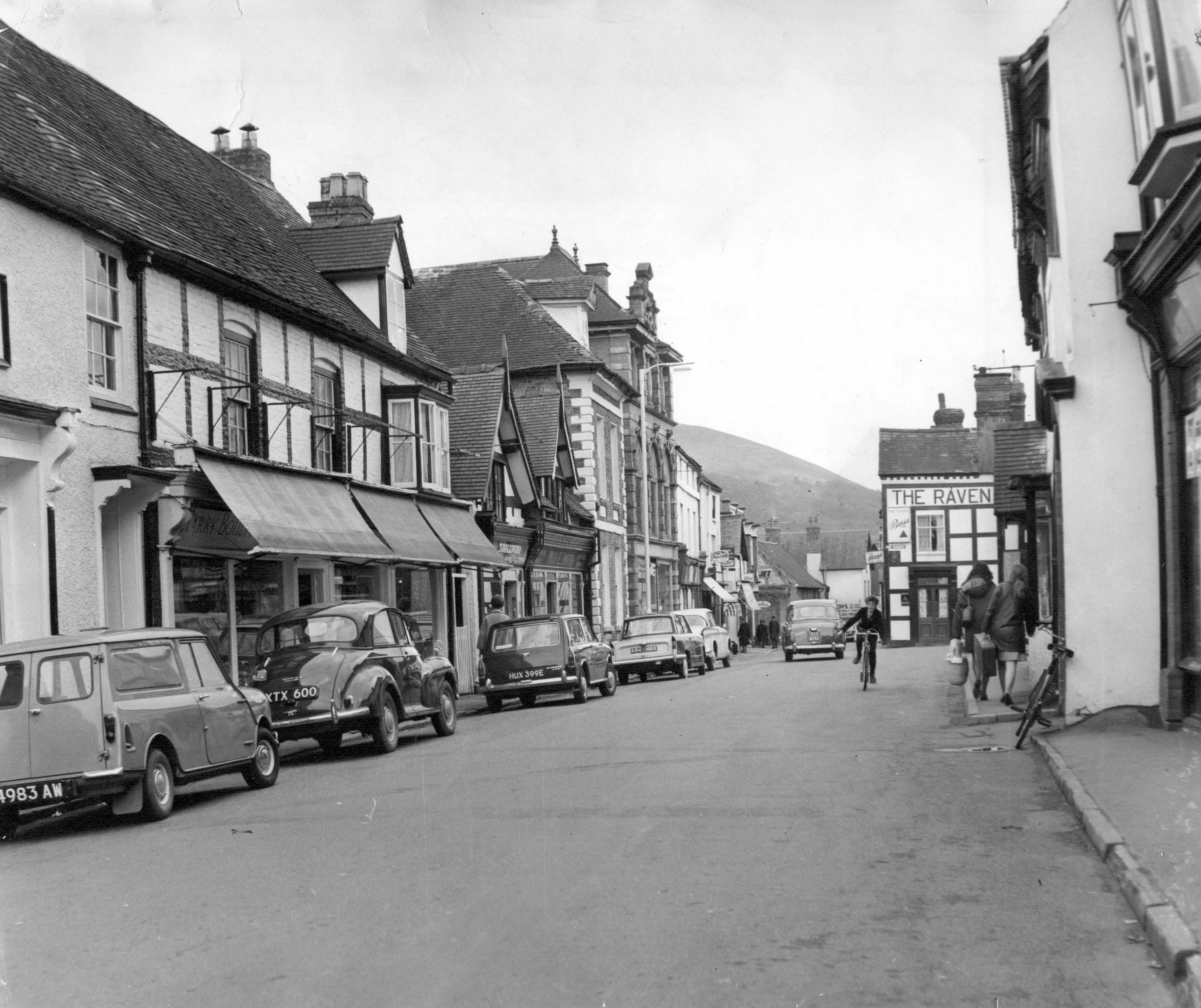 A peaceful scene from Church Stretton High Street in May 1967, when the pace of life seemed a little slower. Parked cars line the street, while a child on a bicycle adds a lovely everyday touch to this snapshot of village life. Do you remember cycling around the town as a child, or the familiar shops and faces that made up the High Street back then?