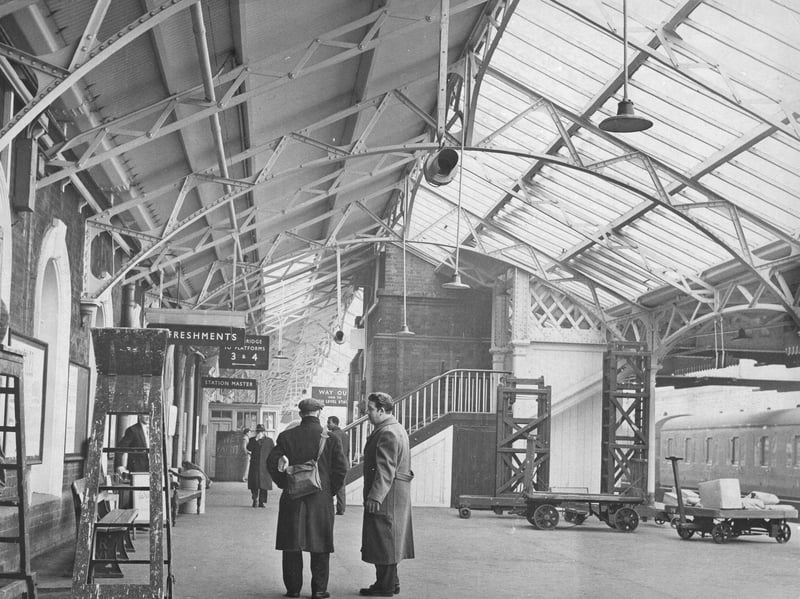 Passengers stand beneath the soaring glass roof of Wolverhampton Low Level station as maintenance workers give the platform a fresh lick of paint in May 1962. The Great Western Railway landmark was given a bright and airy spruce-up as part of its regular upkeep, perfectly timed ahead of Queen Elizabeth II's official visit to the town on May 24. With painted ironwork, clean signage pointing to the refreshments room and station master's office, and heavy luggage trolleys waiting along the platform, this classic photograph captures the bustling railway hub at its absolute best. Do you remember being in town for the Queen's royal visit in May 1962, or taking a train from the Low Level station back in its heyday?