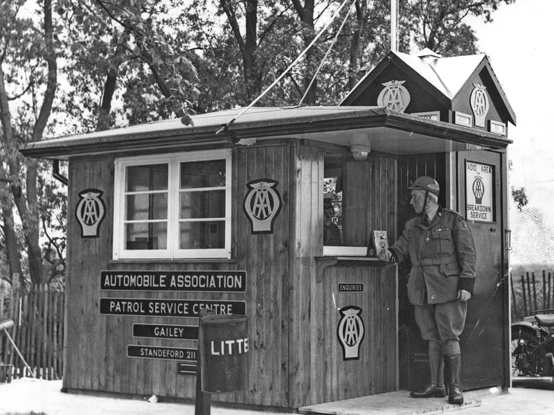 An AA patrolman stands smartly at the enquiry window of a novel, chalet-style patrol service centre in June 1962. Installed at Gailey, this wooden hut was one of the first of its kind in the district, representing a modern upgrade to the Automobile Association's roadside network. Complete with radio breakdown service links, prominent AA insignia, and local signage, these distinctive wooden hubs provided a welcome haven and direct line of help for stranded motorists during the rapid expansion of 1960s road travel. Do you remember pulling over at these wooden AA posts or saluting the patrolmen back in the 1960s?