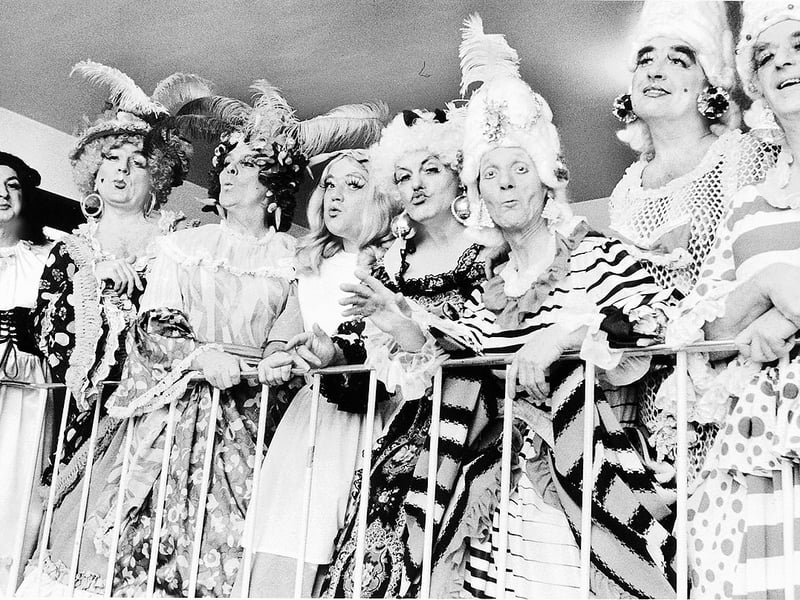 Cast members lean over the balcony railings in full theatrical glamour for the Christmas fantasy pantomime staged at Wolverhampton's Civic Hall in 1982. Dressed in towering feathered wigs, rouged cheeks, and ruffled gowns, the flamboyant ensemble features (left to right) Tony Surman, Bill Jones, Ray Morris, Jim Bridgewood, Ken Herman, Tony Guiness, Tony Westwood, and Denis Grayson. Did you catch this colourful Christmas fantasy pantomime or perform on stage at the Civic Hall during the festive season of 1982?
