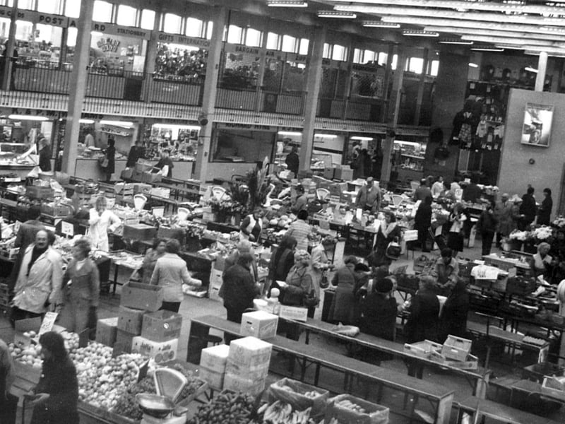 Shoppers thread between fruit and vegetable stalls stacked with wooden produce crates on November 13, 1979, captured in a snapshot by Walter Winder of the Exchange pub and later preserved by resident caretaker Cyril Hughes, who lived high atop the market building. Which market stalls do you remember visiting every week to buy your fresh groceries and treats? Did you know market caretaker Cyril Hughes or ever catch a glimpse of the unique home built right on the roof?