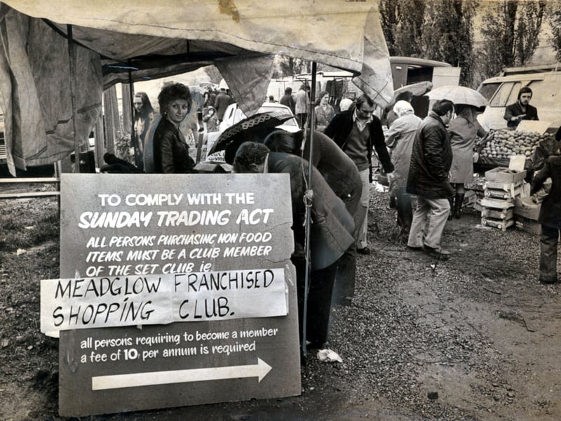 Shoppers browse outdoor market stalls beneath canvas awnings beside an eye-catching directive sign in Dudley Wood in 1974. To navigate the strict restrictions of the Sunday Trading Act, entrepreneurial stallholders devised an ingenious members-only loophole: customers wishing to buy non-food goods joined the "Meadglow Franchised Shopping Club" for an annual fee of 10p, flashing their membership cards whenever making a purchase. Did you ever sign up for the shopping club to grab a weekend bargain, or remember visiting the Dudley Wood market during the mid-1970s?