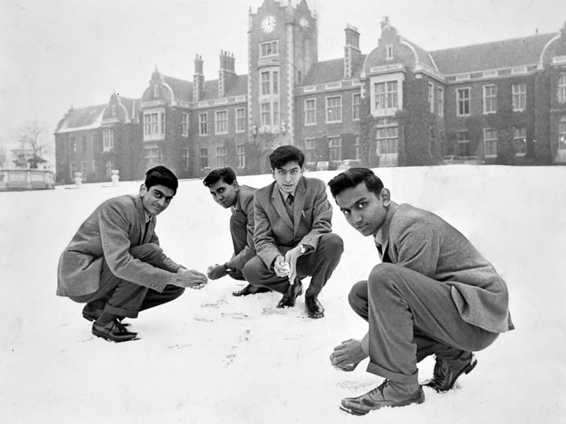 Visiting Zambian students crouch in the fresh snow to make snowballs outside The Royal School, Wolverhampton, during a cold spell in 1966. Smartly dressed in tailored suits, the visiting scholars enjoy a playful moment against the majestic, clock-towered backdrop of the school grounds. Do you remember when foreign exchange students visited local schools in Wolverhampton, or recall experiencing the snowy winter of 1966?