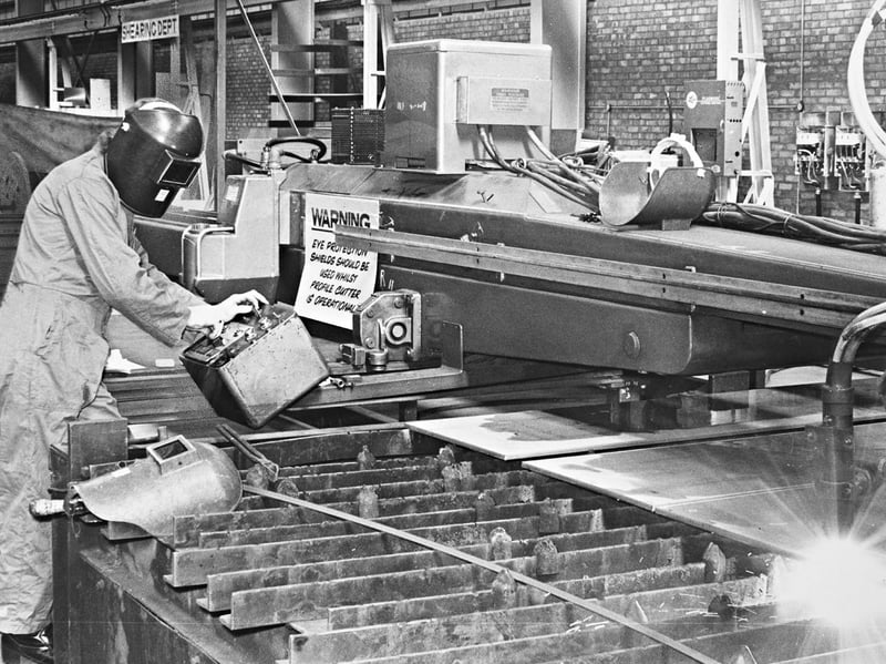 A masked operator monitors an advanced cutting torch in the shearing department at GKN Steelstock in Oldbury in October 1976. Incorporating sophisticated electronics and computer-guided technology, modern profiling machines like this one were capable of cutting intricate, complex shapes across three dimensions with minimal human intervention, showcasing the steady technical evolution of the region's heavy industries. Did you ever work with automated cutting gear or spend time on the shop floor at GKN in Oldbury during the late 1970s?
