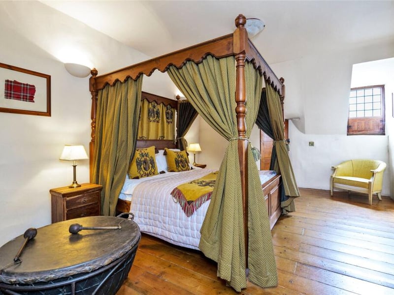  Elevated on a wooden platform, a four-poster bed draped in soft curtains takes centre stage, creating a sense of romance and retreat.
