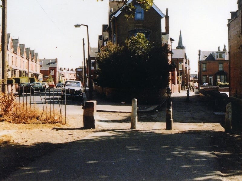 An entrance to Cross Flatts Park looking towards Maud Avenue, left. On the right is a ginnel running between the backs of houses on Maud Avenue and the boundary wall of Cross Flatts school. Houses on Harlech Road are in the background, right, and beyond these the spire of Trinity Methodist Church can be seen.