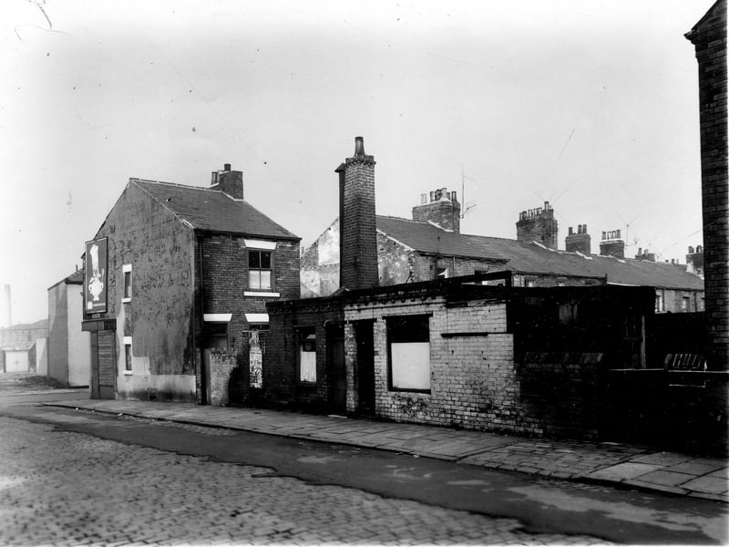 Leek Street in November 1960. On the far left is Glasshouse Street with a boarded up shop on the corner. In the centre of the image are number 22 and 24, two workshops with a chimney on the left of number 24. On the far right is the rear yard of number 52 Mosdale Street, a through terrace.