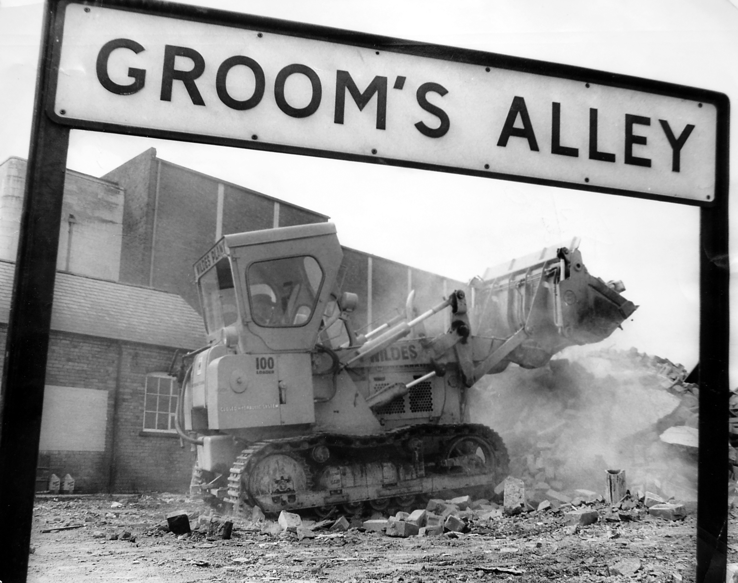 July 1970: Demolition work at Groom’s Alley as a three-storey warehouse is cleared to make way for a supermarket. The scene shows a bulldozer operated by Wildes pushing through the remaining brickwork, with the Clifton Cinema visible in the background. 