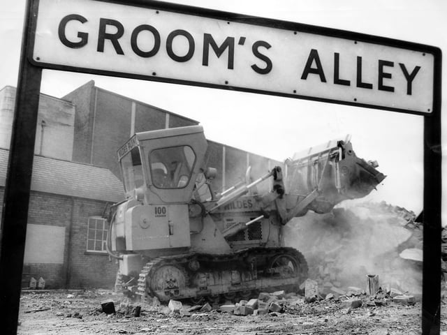 July 1970: Demolition work at Groom’s Alley as a three-storey warehouse is cleared to make way for a supermarket. The scene shows a bulldozer operated by Wildes pushing through the remaining brickwork, with the Clifton Cinema visible in the background.
