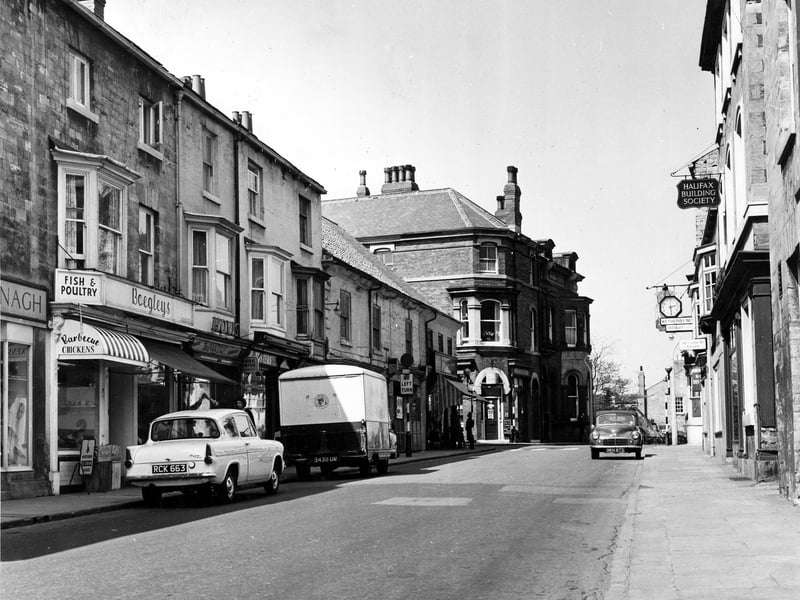 High Street in June 1962. Businesses on the left include, Kavanaghs of Wetherby, footwear retailers at number 31 High Street and Boegley's Fish, Game and Fruit at number 33. At the very right edge, part of the Brunswick Hotel, formerly the Devonshire, at number 22 High Street, is visible. Then there is the Halifax Building Society followed by Crossley's Printers Ltd. and the Wetherby News Offices.