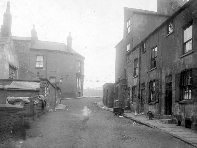 A view Looking up Buslingthorpe Road with Buslingthorpe Place on the left towards junction with Scott Hall Road. The photo from April 1930 shows nos. 1,3 and 5 Buslingthorpe Road (right) - a terrace of 3 storey houses with cellars with taller buildings towards top of row. A pram can be seen on road. Gas Lamp visible on corner.