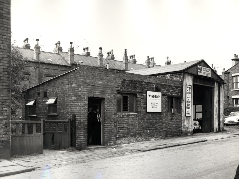 Two commercial properties on Main Road pictured in September 1966. In the centre is Windsors licensed betting office at number 47 with G.B. Motors following to the right at number 51 offering panel beating and cellulose spraying. Two men stand in the door of the bookmakers. In the background are properties on Back Colton Road.