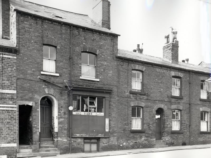 Two back-to-back properties on Main Road, number 19 to the left is a fish and chip shop with an outside light and advertisements for Tizer in the window. Number 21 follows to the right. These buildings were due for demolition in line with slum clearance plans for the city of Leeds. Pictured in September 1966.