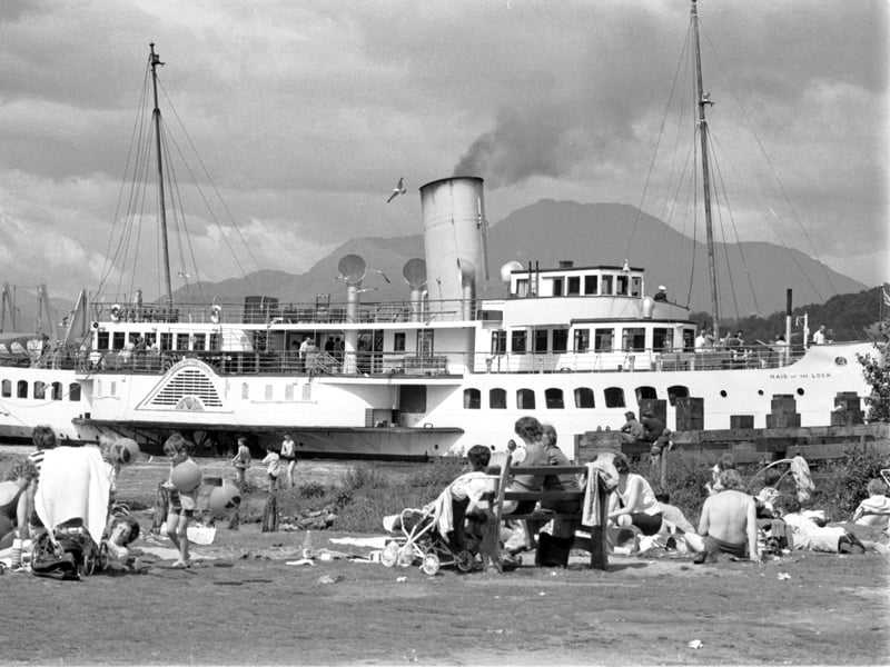 Holidaymakers enjoy the sun in Balloch as the Maid of the Loch paddle steamer passes by in Loch Lomond, in July 1972