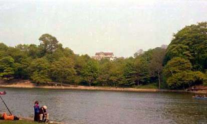 This view looks across Waterloo Lake. In the bottom left corner three people are visible. The view looks in the direction of Hammond Hall Hostel which can be seen on the horizon.
