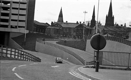 This view looks across the slip road of the Inner Ring Road towards Woodhouse. This is the area where Woodhouse and the City Centre meet. Part of Woodhouse Lane Car Park can be seen on the left edge with the BBC building in the centre. Beyond this are three church spires, Blenheim Baptist Church, Trinity Church and Emmanuel Church left to right.