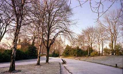 This view looks along a snow covered footpath in Potternewton Park. In the background towards the left is the gatehouse which stood at the entrance to the park from Harehills Lane.