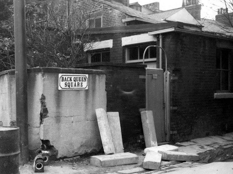 Looking west shows number 18 Back Queen Square in November 1968. A tall, wooden gate and brick wall are in front of the house. Concrete slabs are leaning against the wall. The street sign and an oil drum are visible.