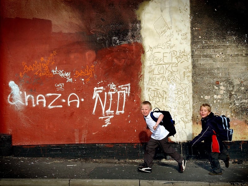 Two children run home from school, in front of a backdrop of graffiti in October 2003.