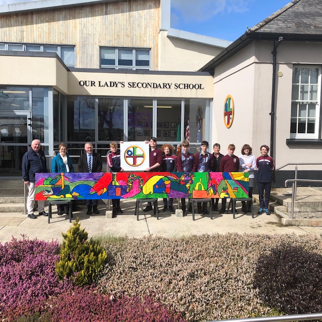 Our Lady's Secondary School -Fin O’ Hara, art teacher in Our Lady’s, had the privilege of assisting our Transition Year students with the “Lions Club Mural”. As a group we thought long and hard on what might we do with this eight by four foot sheet of timber. In the end we took the decision of doing a continuous line of drawing and in order to do this we cut the sheet in two, thus creating a sixteen by two. two foot by sixteen. I challenged the students to find as many images on their phones as they could within five minutes. As the students found the images, I responded by drawing them in one continuous line never lifting the pen. The students then followed me with black paint for the outline. We then turned the picture upside down and randomly filled in spaces with vibrant colours. The thinking behind the piece is to challenge the viewer to identify images hidden within the work. By doing this we are encouraging the viewer to slow down as they enter a place which is designed to slow people down.