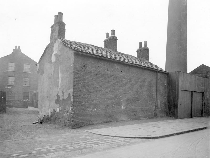 Junction Road in November 1934. Three storey brick house with sign. Back Kidacre Street, appears to be empty, area of cleared ground then back view of property which is brick with slate roof and three chimneys. To right, wooden structure and factory chimney. At this time, the council had declared that this was an unhealthy area.
