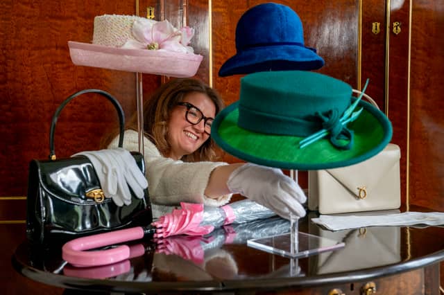 A member of staff from the Royal Trust Collection takes a closer look at a green teal wool hat with in-laid straw emerald green brim, designed by Rachel Trevor-Morgan, that the late Queen Elizabeth II wore for the opening of the 6th session of the Scottish Parliament in October 2021 which is on display at the Palace of Holyroodhouse in Edinburgh, the official residence of the monarch in Scotland.