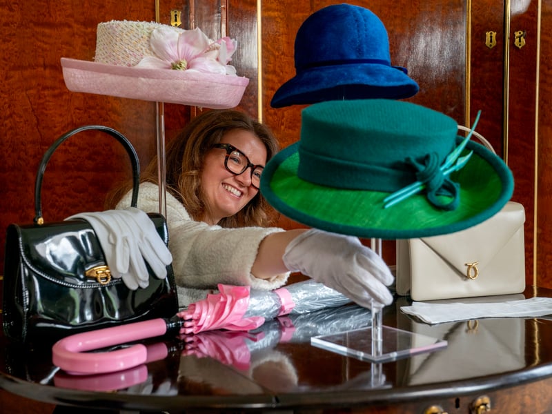 A member of staff from the Royal Trust Collection takes a closer look at a green teal wool hat with in-laid straw emerald green brim, designed by Rachel Trevor-Morgan, that the late Queen Elizabeth II wore for the opening of the 6th session of the Scottish Parliament in October 2021 which is on display at the Palace of Holyroodhouse in Edinburgh, the official residence of the monarch in Scotland.