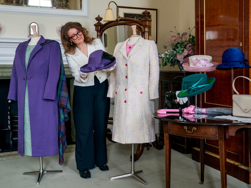 A member of staff from the Royal Trust Collection alongside a green day dress, purple coat and purple trilby hat worn by Queen Elizabeth II for the official opening of the Scottish Parliament in July 1999 and a fine candy pink wool crepe dress with white thick broucle tweed wool coat worn at the Garden Party in 2017, which is on display at the Palace of Holyroodhouse in Edinburgh, the official residence of the monarch in Scotland. 