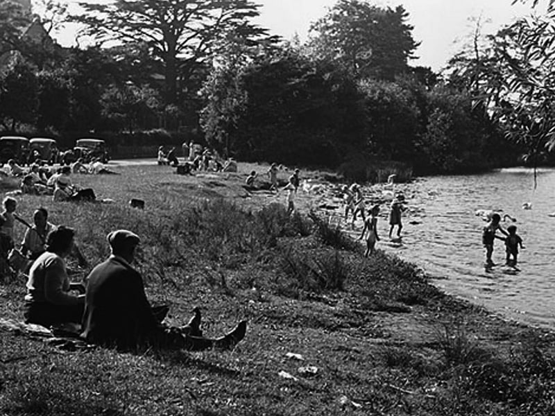 Children and adults cool off at The Mere in Ellesmere during the summer of 1949, with the parish church rising in the background. The photograph captures the relaxed atmosphere of the town’s popular “Lido” area.