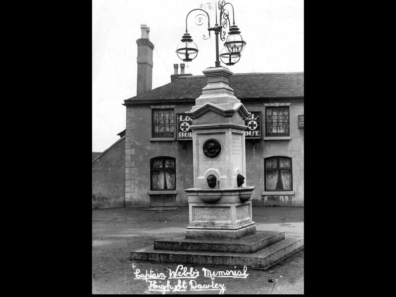 The Captain Webb Memorial stands on High Street, Dawley, with the Lord Hill pub visible in the background. The memorial was erected in 1909, and this undated photograph was taken not long after. The image also shows the original lighting fixtures on top of the memorial, which are no longer present today. The monument commemorates Captain Matthew Webb