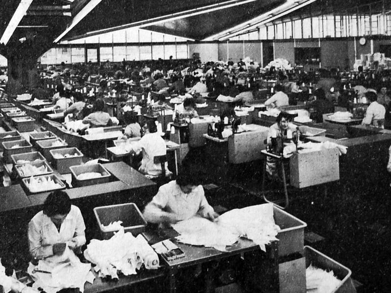 A busy scene inside the Corset Silhouette factory at Towers Lawn, Market Drayton, on November 22, 1963, as employees settled back into their usual workplace after a temporary move to Pell Wall Hall. The relocation had been necessary while problems with the factory roof were addressed, and this photograph captures the workforce back at their machines as normal service resumed.