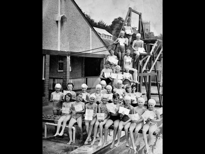 Pupils from Mount Lane Junior School pictured at Market Drayton Swimming Baths, believed to be aged around 9 or 10, sit proudly on the diving board holding their swimming certificates, including “Length” and “Advanced” awards. The print is undated, but thought to date from the 1940s or 1950s.