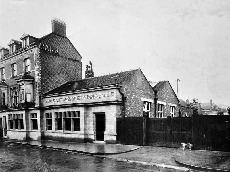 A street scene showing the Market Drayton branch of the London County Westminster & Parr’s Bank Ltd, believed to date from around 1920 at 53 Cheshire Street. The image, held in the National Westminster Bank Archives, carries a handwritten note identifying it as the former Westminster branch. A dog can be seen by the gate in this early 20th-century town scene.