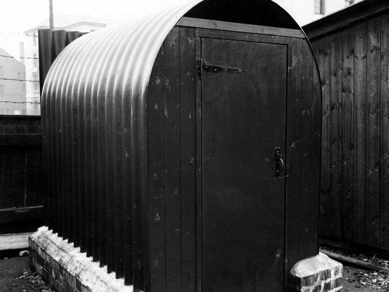 A converted air raid shelter in a back yard. Barbed wire is above the wooden fence behind and a lamp post is in the background. This is likely to be just off St James Street in the grounds of a building used for this purpose. The white building is the Civic Hall on Calverley Street. The building to the left was The Coliseum. Pictured in May 1946.