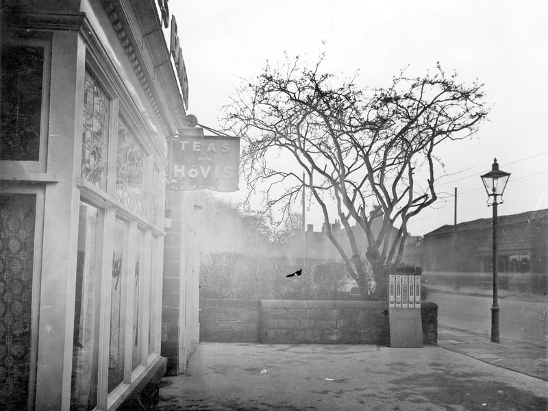 The forecourt of the Swiss bakery at no 46 Otley Road, showing stained glass windows. There is a cigarette machine and a street lamp. Pictured in December 1935.