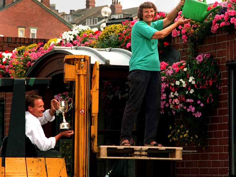 Betty Worsnop waters the flowers from the forklift at Duffield Printers while company chairman Martin Duffield holds the trophy.