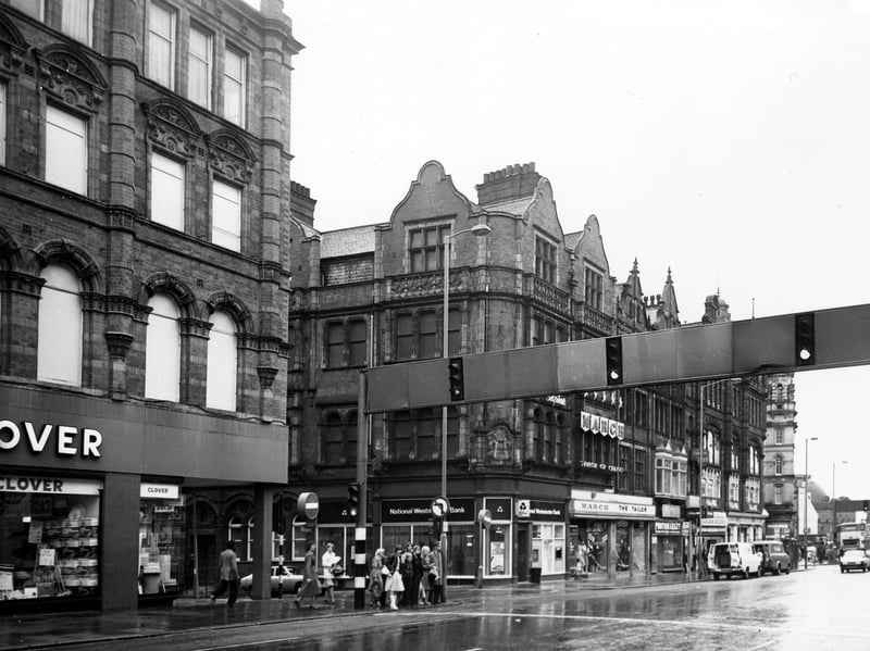Looking across Vicar Lane to the junction with Sidney Street in December 1979 showing from left, Clover department store, National Westminster Bank, March the Tailor, Photomarket and Bargain Records. Several people are waiting to cross the road by the traffic lights.